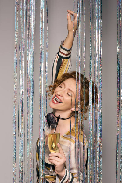 The young woman celebrates joyfully while posing cheerfully, holding a sparkling drink in hand.