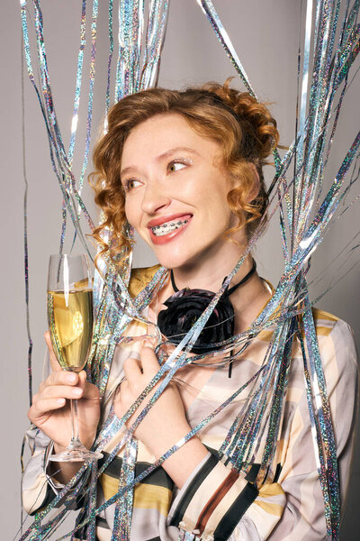 Молодая женщина улыбается с шампанским, окруженная блестящими лентами на празднике.