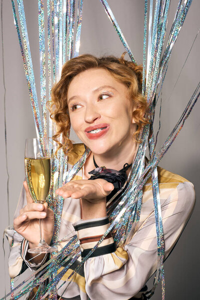 Молодая женщина тепло улыбается, держа в руках игристый напиток среди ярких стримеров.