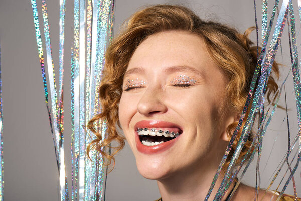 A young woman smiles brightly while posing actively, surrounded by shiny decorations.