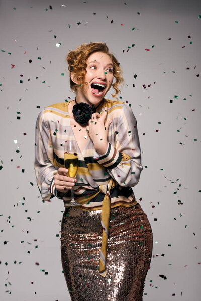 Молодая женщина радостно смеется с игристым напитком, когда вокруг нее падает конфетти..