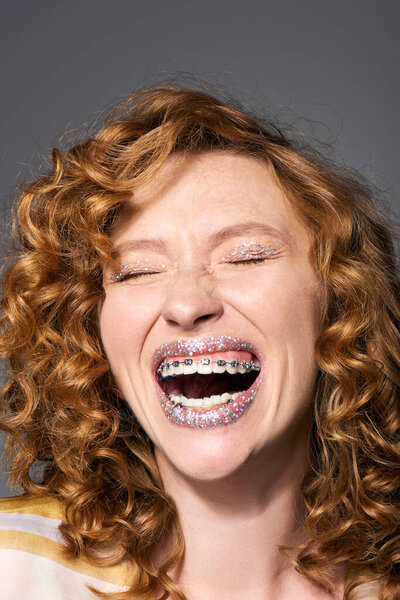 A young woman with curly hair joyfully posing cheerfully, showing off her braces and creativity.