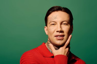 Genç adam cesur yeşil bir arkaplan önünde neşeli bir poz verirken dövmelerini sergiliyor..