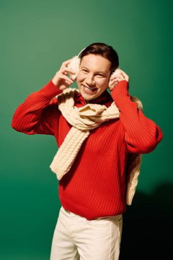 A young man wearing a red sweater and headphones smiles joyfully while listening to music. clipart