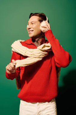 Kırmızı kazaklı genç adam müzikten hoşlanıyor, kulaklık tutuyor ve dövmelerini gösteriyor..