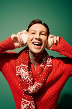 A cheerful young man with tattoos enjoys the winter season, wearing a festive scarf and earmuffs. clipart