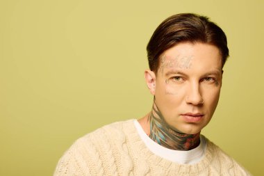 Genç bir adam kamerayı düşünceli bir ifadeyle meşgul ederken benzersiz dövmelerini sergiliyor..