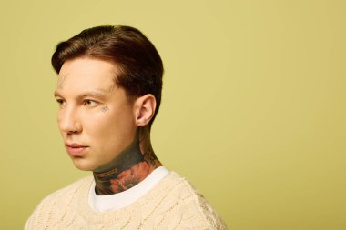 Çarpıcı dövmeleri olan genç bir adam otururken düşünceli bir ifade sergiler..