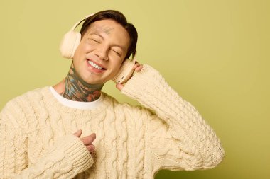 Dövmeli genç bir adam neşeli bir atmosferde müzik dinlerken mutlu bir şekilde gülümser..