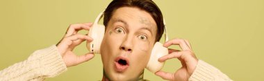 A tattooed young man expresses excitement as he enjoys music with headphones on. clipart