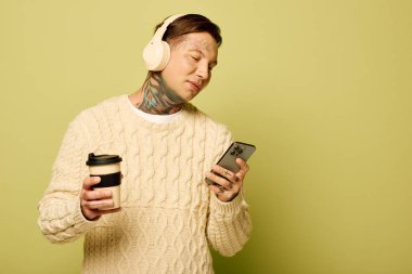 Canlı dövmeleri olan bu genç adam rahatlıyor, kahvesini yudumluyor ve telefonunu kontrol ediyor..