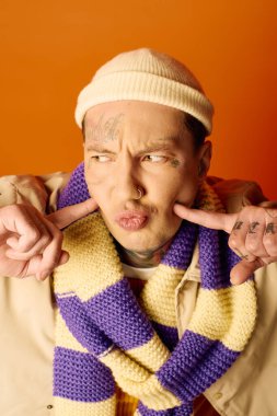 A young man playfully makes a funny face while showcasing his colorful scarf and tattoos. clipart