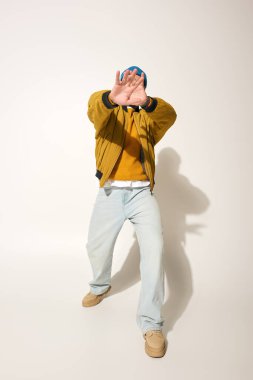 Canlı dövmeleri olan genç bir adam renkli bir ceket giyerken neşeli bir poz verir..