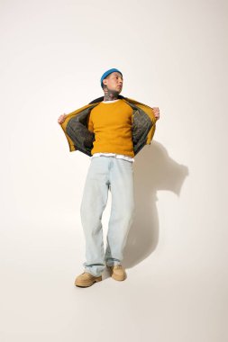 Dövmeleri olan genç bir adam rahat kıyafetini sergiliyor, canlı süveterini gösteriyor.