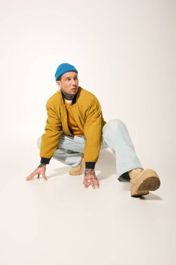 Dövmeli bir genç adam, günlük kıyafetler giyerken arka planda yaratıcı bir şekilde poz verir..