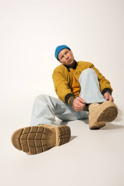 Genç adam dövmelerini ve şık kıyafetlerini sergiliyor, rahat bir şekilde oturuyor ve nişanlı..