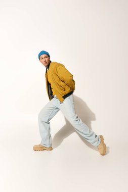 A young man wearing a yellow jacket and blue beanie poses dynamically in a stylish outfit. clipart