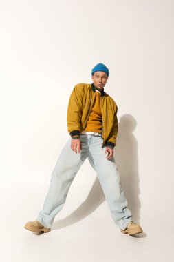 Dövmelerle süslenmiş genç bir adam canlı bir kıyafet ve stüdyoda kendine güvenen bir duruş sergiliyor..