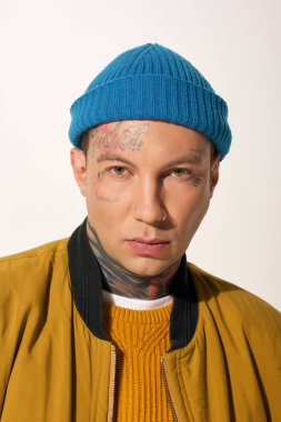 Tattooed young man in a bright hat shows off his unique style against a light background. clipart