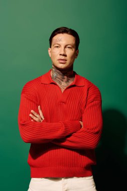 A young man with detailed tattoos stands confidently, wearing a red sweater and white pants. clipart