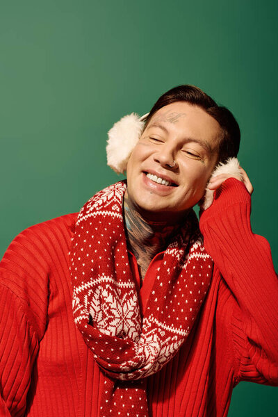 A young man wearing a red sweater and festive scarf smiles happily against a green backdrop.