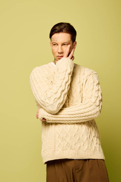 A young man with tattoos appears contemplative in a cream sweater, highlighting his casual style.