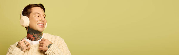 Радостный молодой человек с видимыми татуировками слушает музыку, демонстрируя свое счастье и стиль.