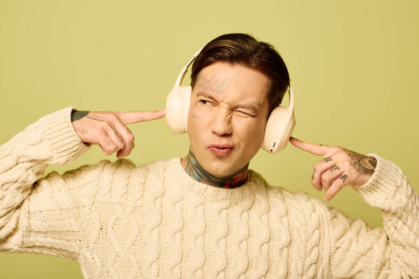 Молодой человек с татуировками игриво слушает музыку в наушниках, радостно улыбаясь.