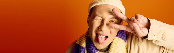 Татуированный молодой человек делает игривый жест, улыбаясь на ярком фоне..