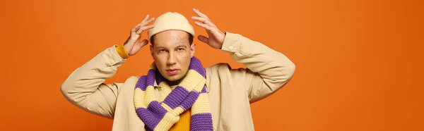 Молодой человек настраивает свой шарф с видимыми на руках татуировками, обрамленными оранжевым фоном.
