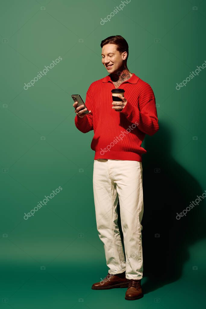A young man smiles while checking his phone and holding a coffee, bright colors surrounding him.