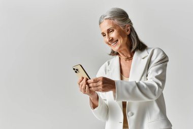 Gri saçlı, şık, olgun bir kadın. Akıllı telefonunu tutarken gülümsüyor. Zarafet ve zarafet saçıyor..