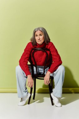 A beautiful mature woman with grey hair wears a red sweater, artistically posing on a green background. clipart