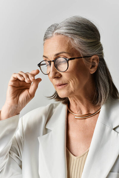 Изысканная женщина с седыми волосами демонстрирует свою элегантность в шикарном белом костюме и очках, излучая уверенность.
