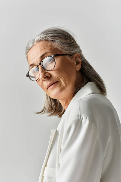 Сложная зрелая женщина с седыми волосами источает уверенность, одетая в шикарный белый костюм.