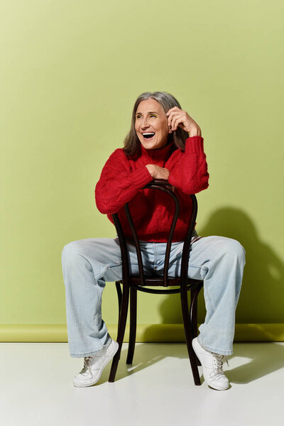 Веселая женщина в ярко-красном свитере излучает тепло и стиль к зеленой стене.