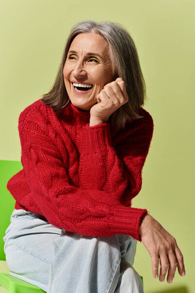 Красивая зрелая женщина с седыми волосами тепло улыбается, демонстрируя зимнюю моду в уютном красном свитере.