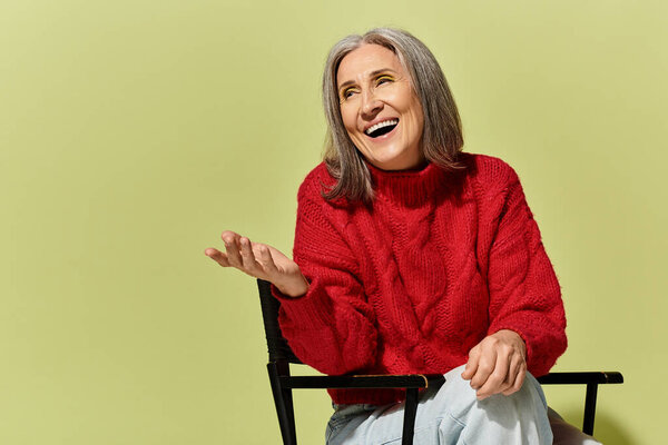 Веселая женщина с седыми волосами радушно улыбается во время зимней обстановки в уютном красном свитере.