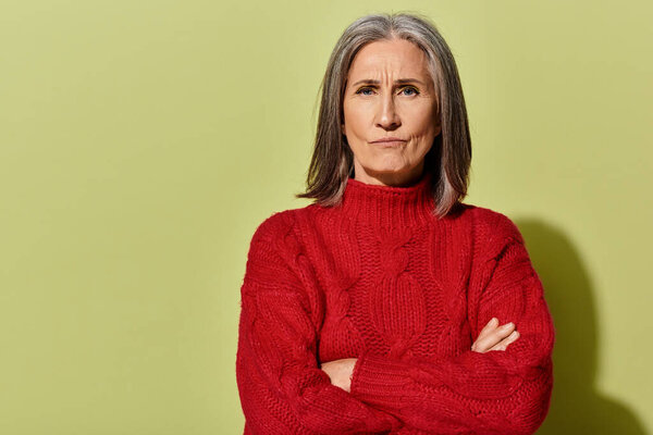 Красивая женщина с седыми волосами носит красный свитер, демонстрируя зимнюю моду в ярко-зеленой обстановке.