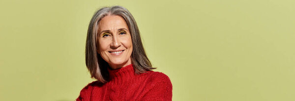 Светлая зрелая женщина с яркими седыми волосами тепло улыбается, одетая в красный свитер, излучая зимнюю элегантность..