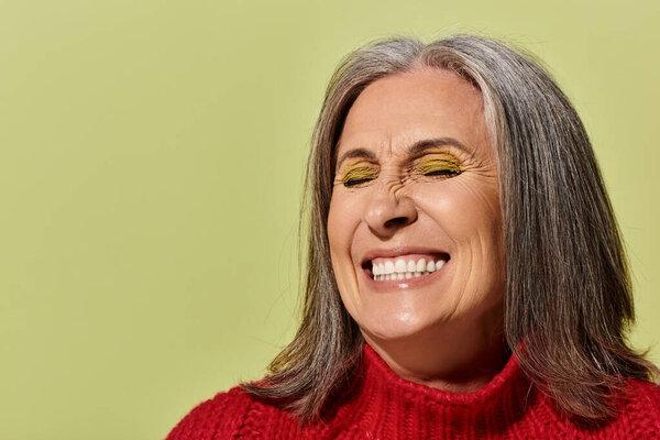 Веселая зрелая женщина с седыми лучами волос в красном свитере, прекрасно олицетворяющая зимний стиль.