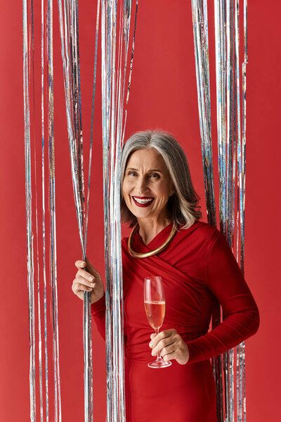 Светлая женщина с седыми волосами празднует Новый год, держа стакан шампанского среди праздничных украшений.