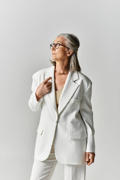 Утонченная зрелая женщина излучает уверенность в белом костюме, демонстрируя свою грацию и стиль.