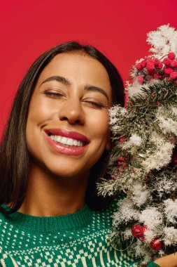 A young woman radiates happiness while holding a festive decoration adorned with berries. clipart