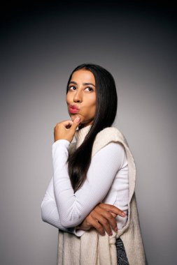 Genç ve güzel bir kadın düşünceli bir şekilde poz verir. Parmağı dudaklarında, derin bir yansımada kaybolur..