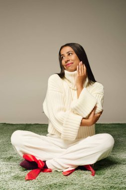 Şık giyinmiş genç bir kadın yeşil bir halıda dinleniyor, düşüncelere dalmış..