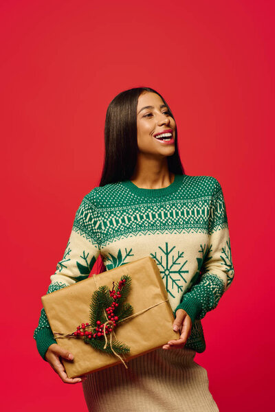 A joyful young woman smiles as she presents a beautifully wrapped gift for the holidays.