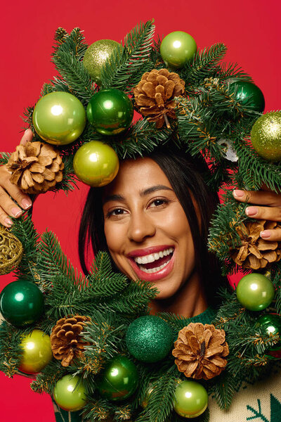 A cheerful young woman holds a decorated holiday wreath, exuding joy and seasonal spirit.