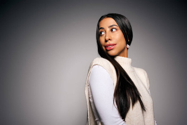 Молодая женщина демонстрирует уверенное выражение лица, слегка поворачивая голову, вызывая любопытство..