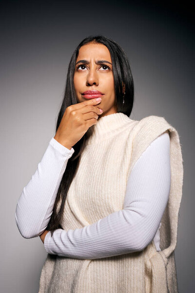 A young woman in a soft sweater ponders deeply, lost in thoughtful reflection within a calm setting.